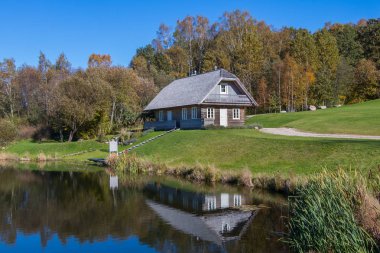 Sonbahar ormanının arka planındaki göletin yanında bir ev.