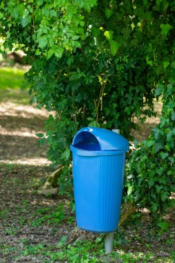 Güneşli bir öğleden sonra bir kamu bahçe üzerinde mavi plastik çöp kovası