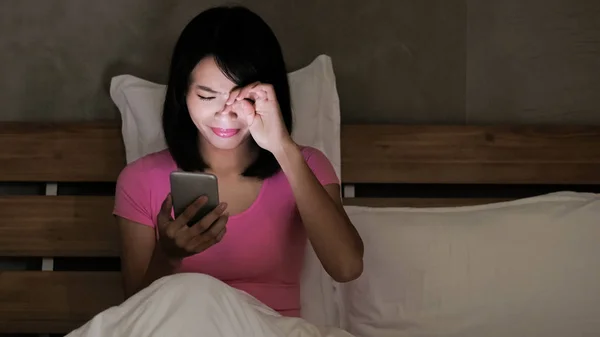 夜ベッドの上の目の問題で電話をしている女の人 — ストック写真