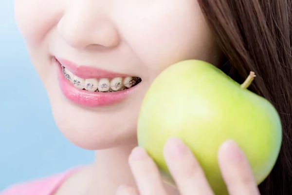 close up woman wearing  braces and holding  apple on the blue background