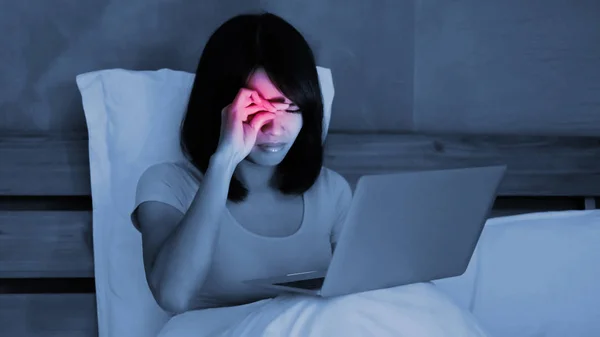 woman using  notebook with eye problem on the bed at night