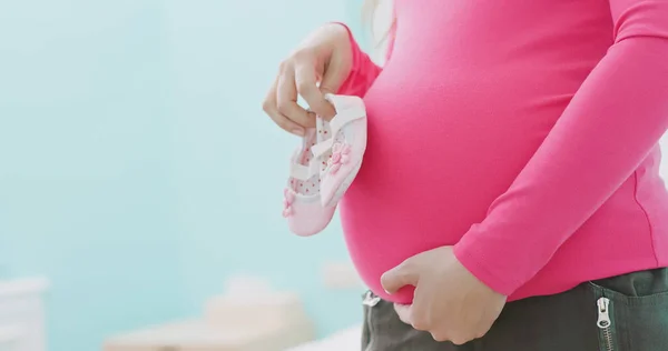 Schwangere Hält Kleine Babyschuhe Und Setzt Sich Auf Das Bett — Stockfoto