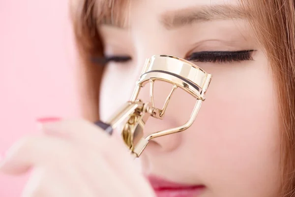 woman  clipping  eyelashes  on the pink background