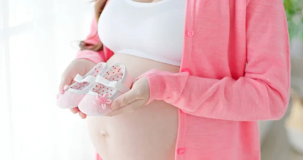 Schwangere Steht Und Hält Kleine Babyschuhe — Stockfoto