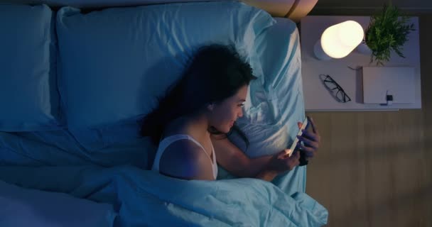 女性はベッドの上でスマートフォンを使い — ストック動画
