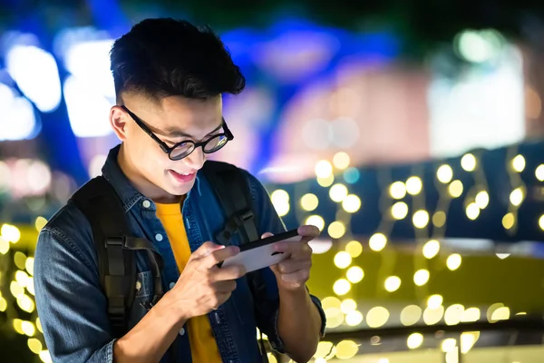 asian young man paly mobile games on smart phone outdoor in the evening