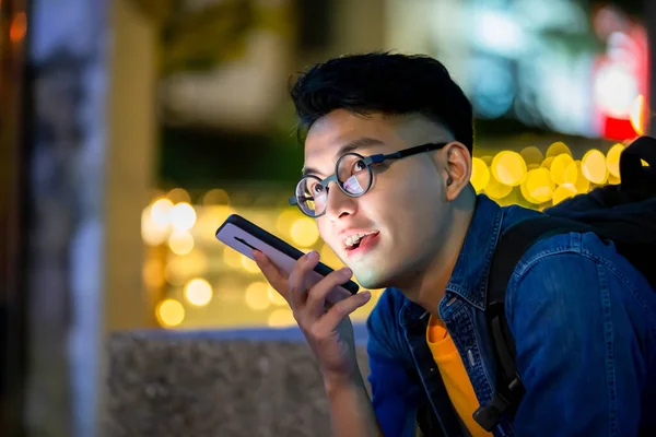 asian young man send vocal messages or use voice assistant outdoor in the evening