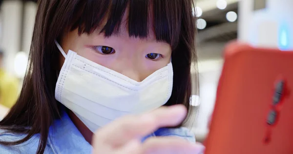 little asian girl use smartphone and wear face mask in the crowd