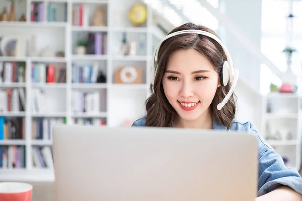 聪明的亚洲女学生使用耳机在网上学习一些东西 并通过家里的笔记本电脑搜索信息 — 图库照片