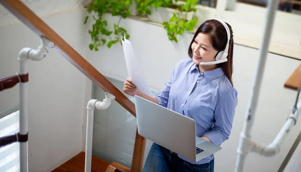 远程工作概念 亚洲妇女阅读财务报告 并使用带耳机的计算机参加家庭视频会议 — 图库照片
