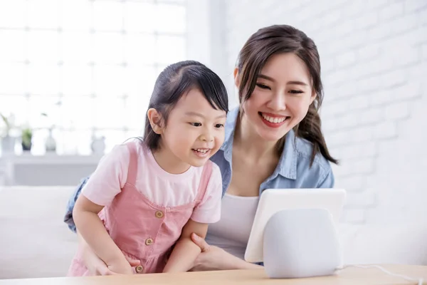 Smart AI speaker concept - Mom and daughter talk to voice assistant with screen at home happily
