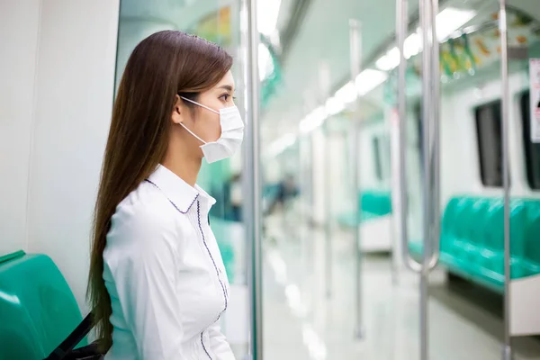 Asian business woman with surgical mask face protection and keep social distance while commuting in the metro or train