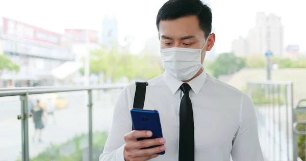 アジアのビジネスマンは顔のマスクで歩きながらスマートフォンを使う — ストック写真