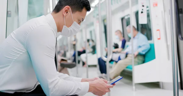 手術用マスク顔保護を持つアジアのビジネスマンは スマートフォンを使用し 地下鉄や電車に通勤しながら 群衆に社会的距離を保ちます — ストック写真