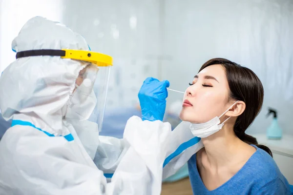コロナウイルス検査 隔離されたガウンや保護スーツや外科的フェイスマスクを持つ潜在的に感染した女性からコロナウイルスサンプルのためのスワブを取っている医療従事者 — ストック写真