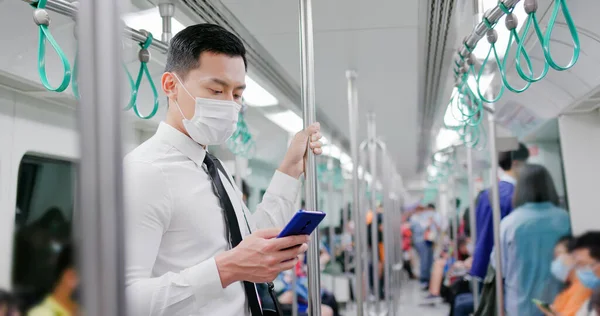 마스크를 아시아 사업가는 지하철이나 기차를 출퇴근하는 스마트폰을 사용하고 사교적 거리를 — 스톡 사진