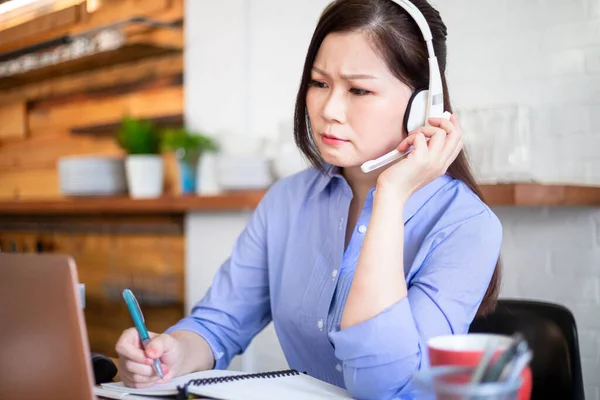 远程办公的概念 亚洲女人用电脑和耳机话筒参加一个视频会议 并对家里的事情感到烦恼 — 图库照片