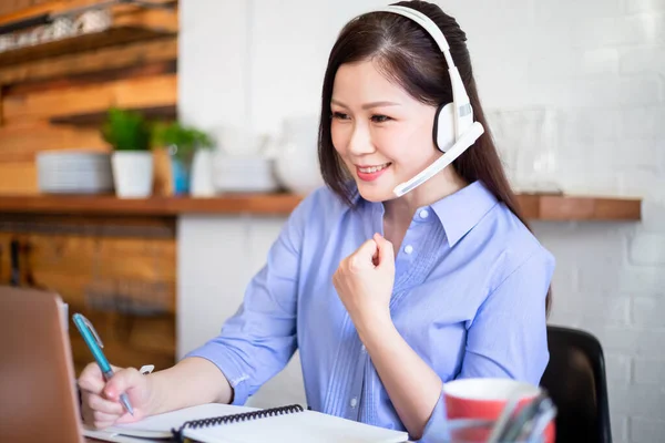 远程办公理念 亚洲女性使用电脑和耳机话筒参加视频会议 并对家里的商业成功感到兴奋 — 图库照片