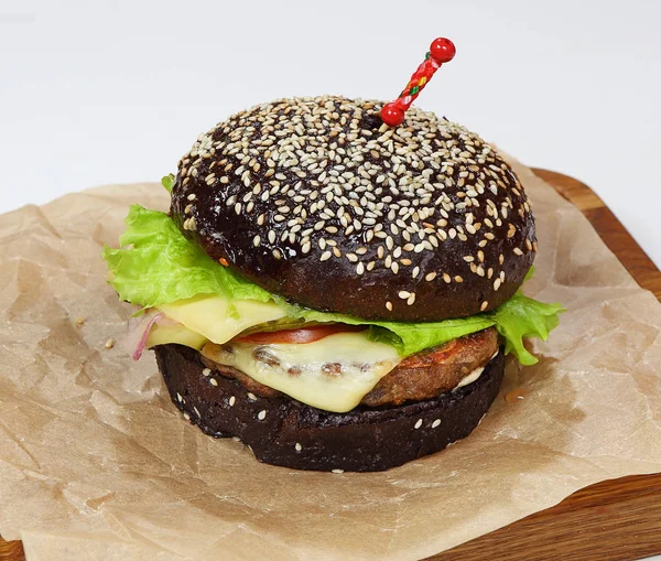 Tasty black burger sprinkled with sesame seeds with chicken, salad, cheese and sauce — Stock Photo, Image