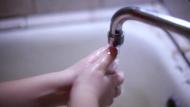 Çocuk ellerini musluk suyunun altında sabunla iyice yıkıyor.