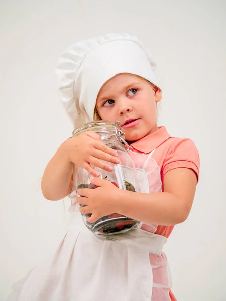 A girl in an apron and a chef\'s hat with a jar in her hands. There are many different berries in the jar. Positive emotions.