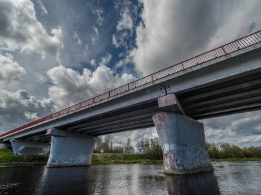 Fırtınalı bir gökyüzünün altında nehir üzerinde yol köprüsü. Ufkun ötesine giden yol.