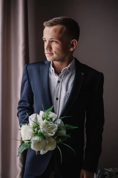 Junger Mann im Anzug mit Blumenstrauß schaut aus dem Fenster — Stockfoto