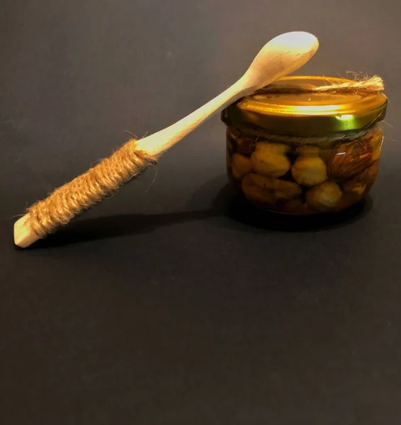 Colher de madeira com um pote de mel com nozes em um fundo preto — Fotografia de Stock