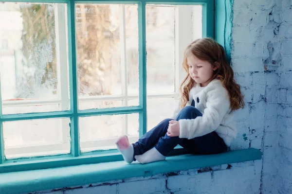 Kleines Mädchen sitzt auf der Fensterbank am Fenster — Stockfoto