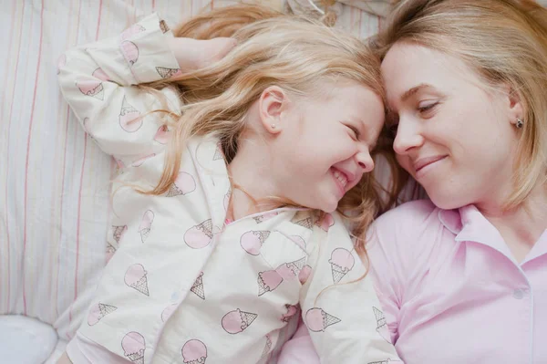 Mother and daughter lying on bed in pink pajamas — Stock Photo, Image