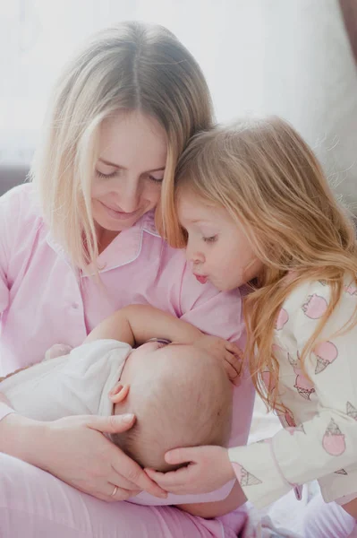 Mamá rubia con hija mayor mira a la hermana recién nacida Imágenes de stock libres de derechos