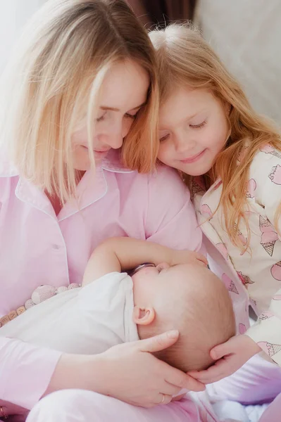 Blondine mit älterer Tochter schaut die neugeborene Schwester an und lächelt Stockbild
