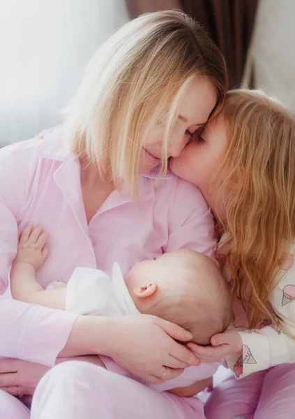 Mãe loira com filha mais velha olhar para o bebê recém-nascido irmã e sorriso Imagem De Stock