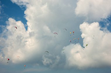 Arka planı bulutlar gökyüzünde paraşütler büyük bir grup uçar.