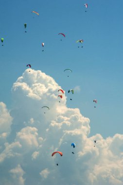 Arka planı bulutlar gökyüzünde paraşütler büyük bir grup uçar.