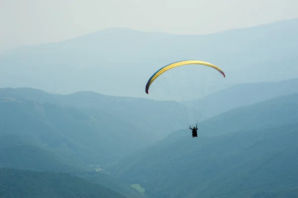 Een paraglider vliegen over een bergdal op een zonnige zomerdag. — Stockfoto