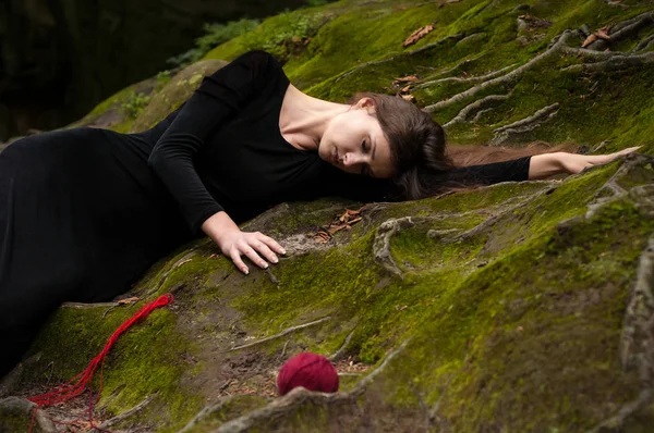 Bir esmer yeşil yosun ve çevresinde kırmızı iplik dağınık topları yatıyor siyah elbiseli portresi.