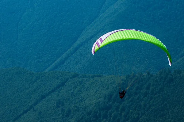Um parapente voa sobre um vale de montanha em um dia ensolarado de verão . — Fotografia de Stock