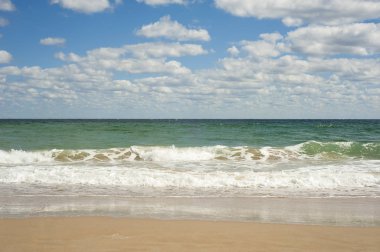Kumlu sahilde mavi deniz dalgası. Güneşli bir yaz gününde bulutlarla birlikte mavi gökyüzü üzerinde güzel deniz dalgaları.. 