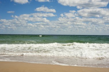 Kumlu sahilde mavi deniz dalgası. Güneşli bir yaz gününde bulutlarla birlikte mavi gökyüzü üzerinde güzel deniz dalgaları.. 