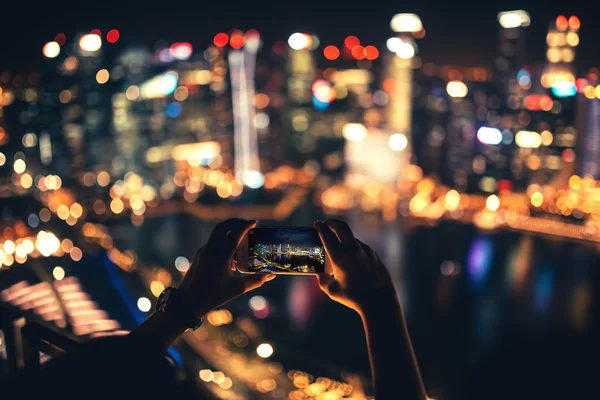 silhouette of woman using smartphone for taking pictures of city skyline at night
