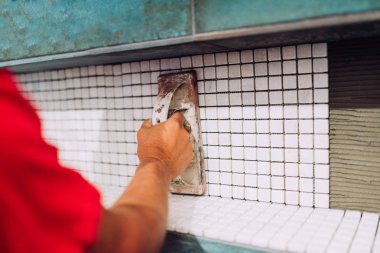 industrial worker applying mosaic ceramic pattern tiles on bathroom shower area clipart
