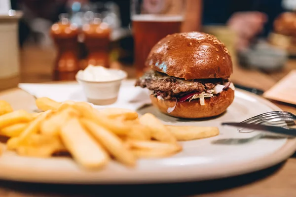 Leckere gegrillte Rindfleisch-Burger mit Salat und Mayonnaise auf weißem Teller mit Pommes serviert. modernes Abendessen mit Burger und Pommes — Stockfoto