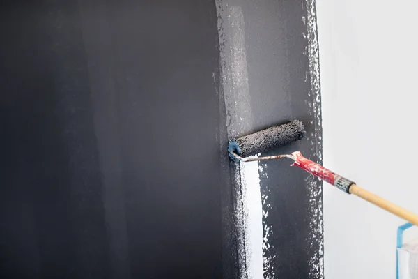 Trabalhador da construção civil pintura paredes cinzentas usando rolo de pintura. Detalhes de design de interiores, renovação e parede de reboco — Fotografia de Stock