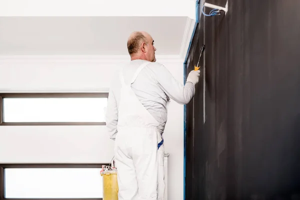 Homem careca, trabalhador usando ferramentas para decorar uma parede com tinta cinza — Fotografia de Stock