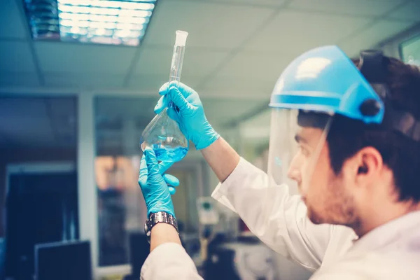 Tubo de ensayo del matraz en manos científicas. Detalles del joven médico analizando la composición y estructura del líquido azul —  Fotos de Stock