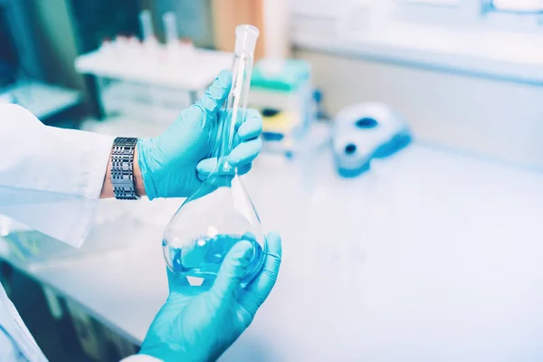 Doctor sosteniendo un tubo de ensayo de vidrio, un frasco con líquido azul en un laboratorio especial preparándose para experimentos —  Fotos de Stock