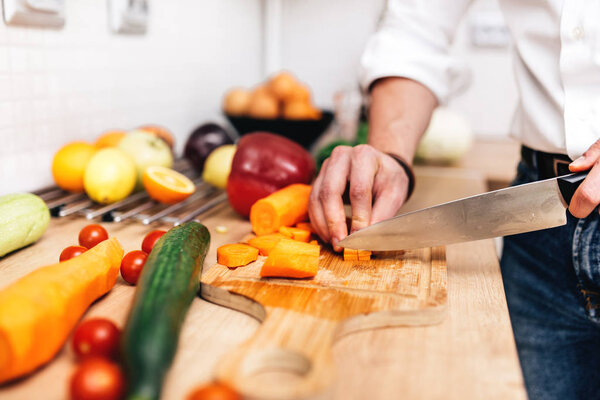 close up details of handsome male chopping vegetables with knife. Professional cook preparing salad