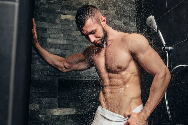 Senza maglietta, uomo muscoloso sotto la doccia nel bagno moderno — Foto Stock