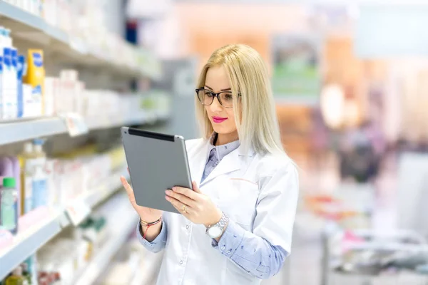 Portrait of pharmacist chemist woman standing in pharmacy drugstore, smiling and using table — Stock Photo, Image